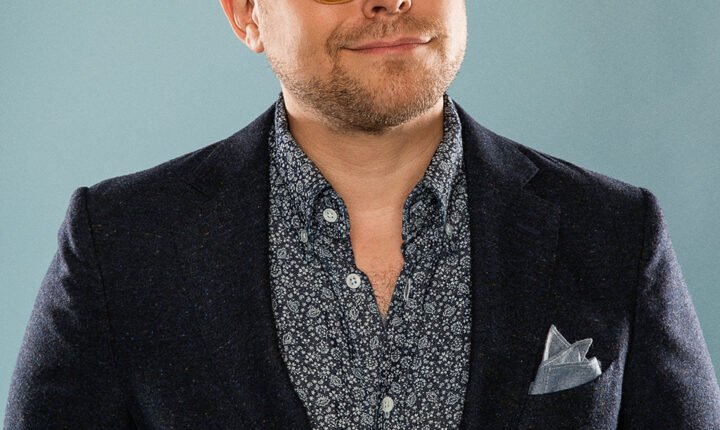 Comedian and YouTuber Adam Conover wearing glasses and a blue suit