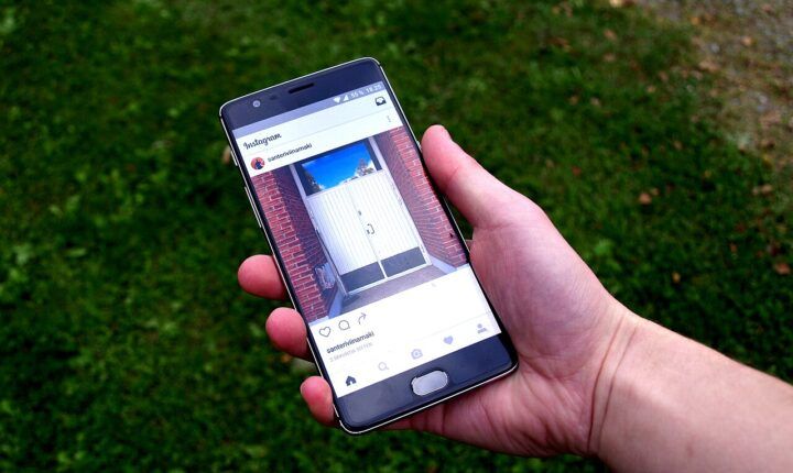 A hand holding a smartphone displaying an Instagram feed above grass in September 2016
