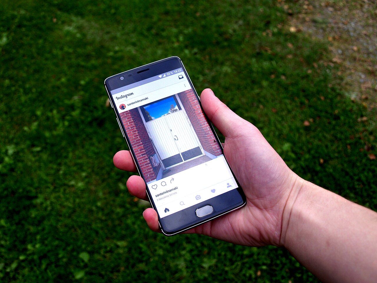 A hand holding a smartphone displaying an Instagram feed above grass in September 2016