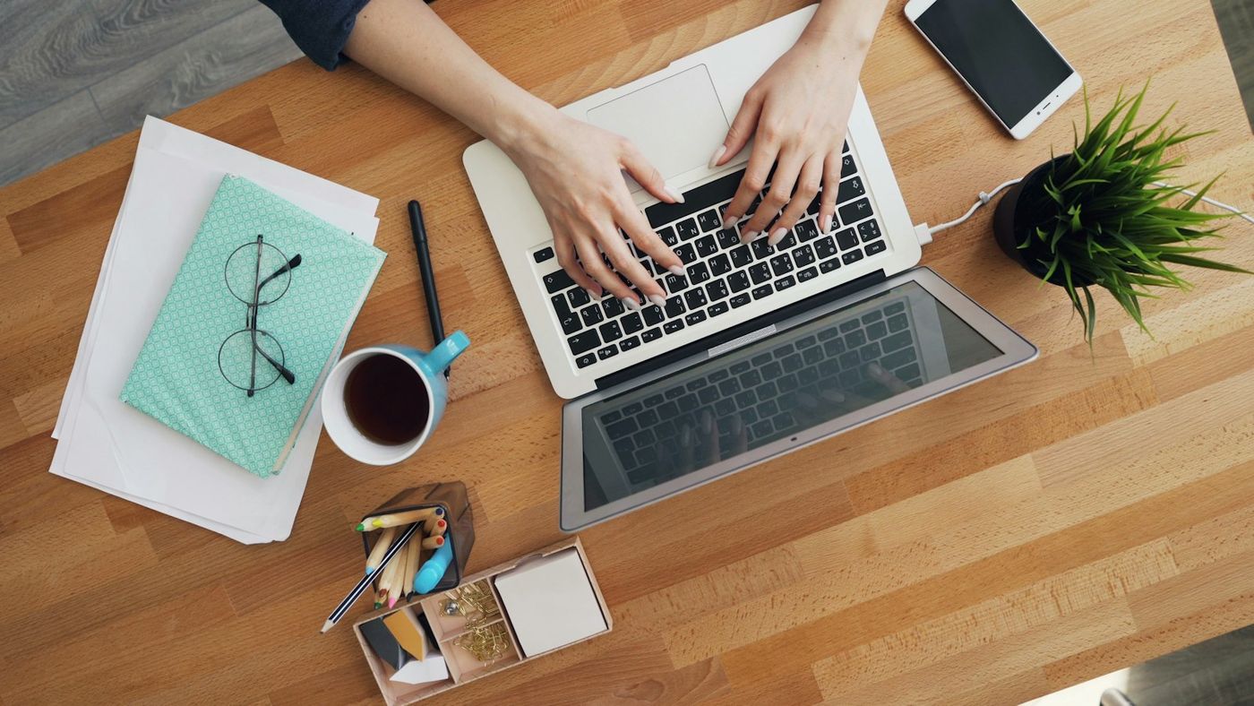 Hands typing on a laptop at an office desk, illustrating newsletter publishing work