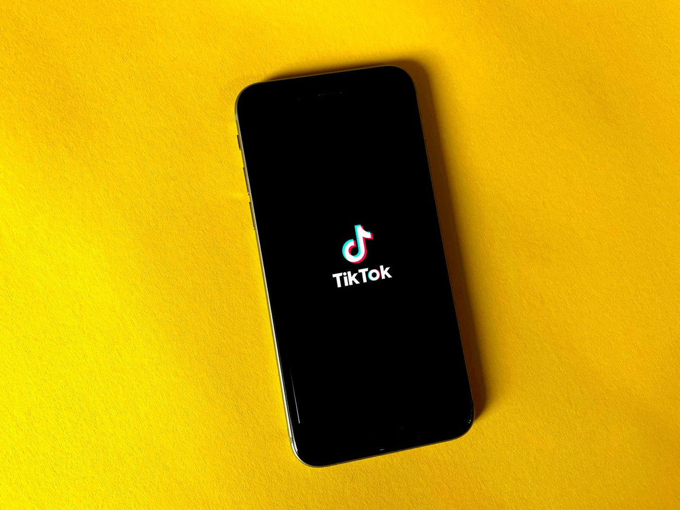 TikTok logo displayed on a smartphone against a yellow background