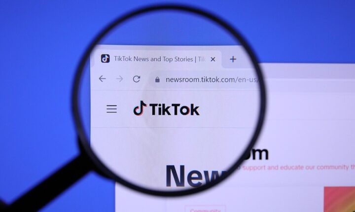 TikTok website logo viewed through a magnifying glass on a computer screen