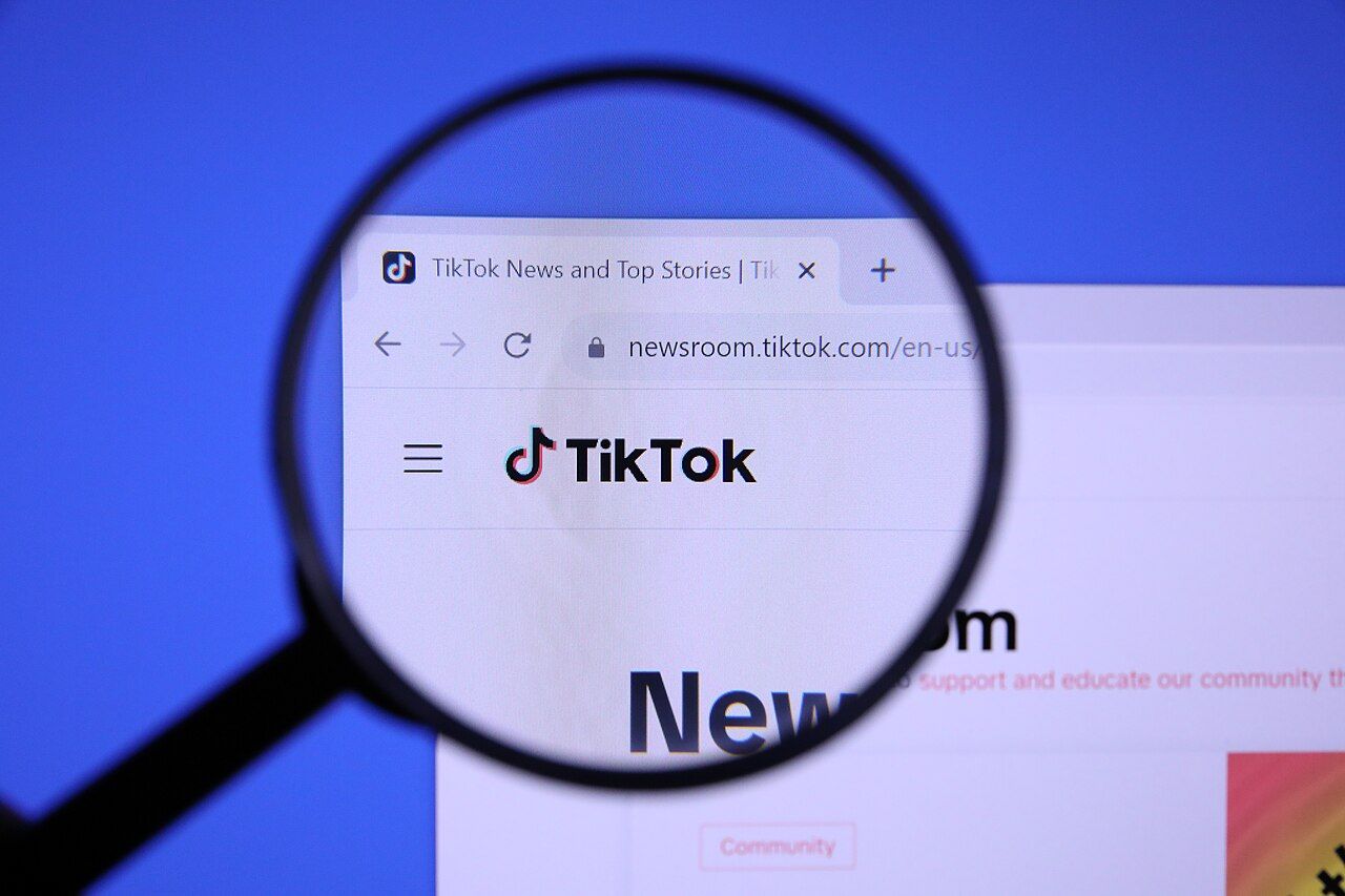 TikTok website logo viewed through a magnifying glass on a computer screen
